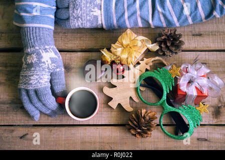 Topview touristische tragen Sie Handschuhe und heißen Kaffee Tasse auf Holz Tisch, die Geschenke Weihnachten Thema dekorieren halten Stockfoto