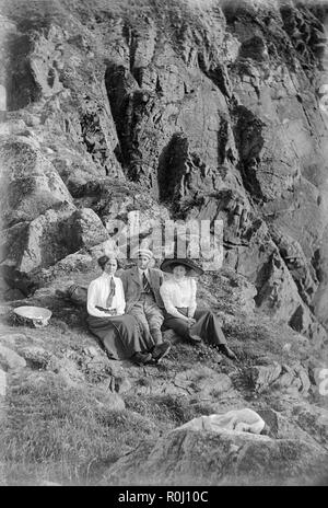 Edwardian schwarz-weiß Foto, ein junger Mann und zwei junge Frauen, sitzen auf dem Boden einer felsigen Klippe, irgendwo in England. Alle tragen Kleidung in guter Qualität der Ära. Eine Frau trägt einen sehr großen Hut, typisch für die edwardianische Zeit. Stockfoto