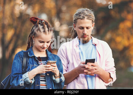 Zwei hipster beste Freunde mit dreads legere Kleidung Nachrichten auf ihren Smartphones und nicht achten auf jedes andere, im Freien. Stockfoto