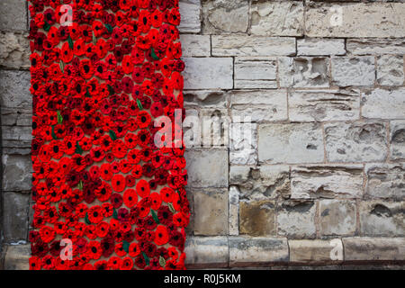 Handgefertigt aus Gewirken und Gestricken Mohnblumen schmücken die Mauer einer Kirche der Hundertjahrfeier der Welt Krieg 1 zugunsten der Poppy Appell zu gedenken. Stockfoto