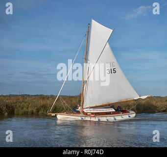 Eine gebrochene Sloop Segelboot mit weissen Segeln auf dem Fluss Thurne, die auf einem klaren Herbstmorgen, Norfolk Broads, Norfolk, England, Großbritannien Stockfoto