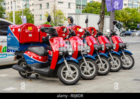 Rot und Blau Dominos Lieferung moped Roller ordentlich in einem Leitung geparkt auf einem Gehsteig in Seoul, Südkorea. Stockfoto