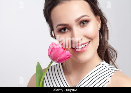 Porträt der jungen brunette schöne Frau mit Make-up in gestreiften Kleid, stehend und Holding pink tulip und Kamera mit toothy Lächeln. indo Stockfoto