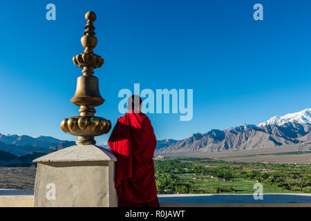 Ein rot gekleideter Mönch hinunter zum grünen Indus Tal Blick vom Dach der Thiksey Gompa, eines der wichtigsten Klöster in Ladakh. Stockfoto