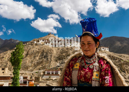Eine ladakhi Frau zeigt ihre traditionelle Kleidung, Lamayuru Gompa und blauer Himmel mit weißen Wolken im Hintergrund Stockfoto