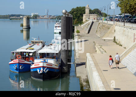 Ein paar Touristen zu Fuß entlang der Ufer der Rhone mit Kreuzfahrtschiffen oder Schuten festgemacht am Kai Arles Provence Frankreich Stockfoto