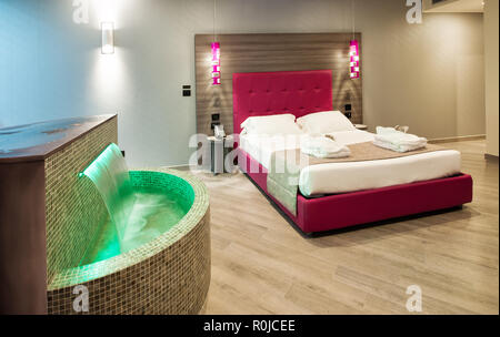 Moderne motel Schlafzimmer in einer luxuriösen Suite mit grünen Fliesen- Wasser und ein Doppelbett mit beleuchteten Lampen und Kopfteil Stockfoto