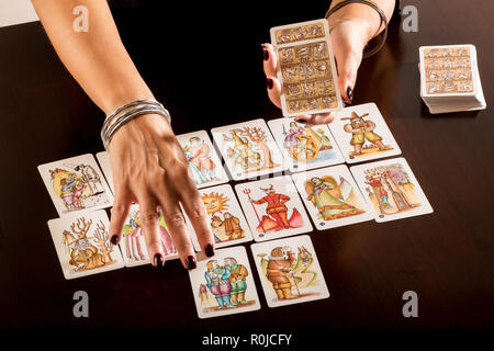 Wahrsagerin verlegen ein Deck der Tarot Karten, wie sie prognostiziert die Zukunft für einen Kunden in der Nähe zu sehen, auf der bildhaften allegorische Karten und Ihr Stockfoto
