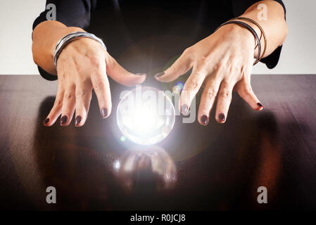 Hellseher oder Wahrsager mit einer glühenden Crystal Ball oder Kugel auf einem glänzenden Holztisch in der Nähe zu sehen, der ihre Hände zum Ausdruck Stockfoto