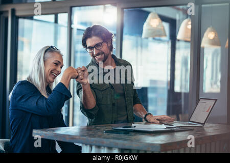 Ein junger Geschäftsmann und eine ältere Geschäftsfrau machen im Büro eine Faust. Geschäftskollegen, die nach Abschluss des Projekts glücklich und begeistert sind. Stockfoto