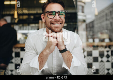 Mann in einem Cafe sitzen in entspannte Stimmung und lächelnd. Lächelnd Mann an einem Tisch im Restaurant sitzen mit Hand an sein Kinn. Stockfoto