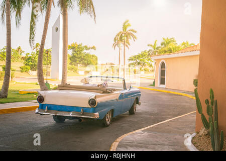 Vintage Classic American blu Auto, Fahrer mit Cowboyhut, während er mit seinem alten amerikanischen Auto auf dem Parkplatz des Hotels verlässt. Stockfoto