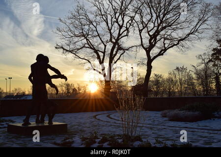 Timeline der aufgehenden Sonne im Winter Sonnenuntergang Himmel aus gesehen hinter dem Bronze Skulptur auf dem Soldatenfriedhof reimsbach an der Saar, Deutschland. Stockfoto