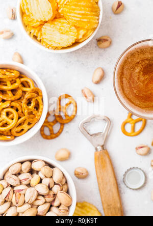 Glas Handwerk Lagerbier mit Snack auf Stein Küche Hintergrund. Brezeln und Chips und Pistazien aus weisser Keramik Schüssel Stockfoto