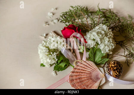 Zarter Bouquet weißer Hortensien mit einem Bud der roten Rose auf einem Zweig von Eukalyptus und Muscheln auf hellem Holztisch Stockfoto