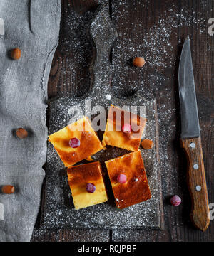 Vier quadratische Scheiben von Hüttenkäse und Pumpkin Pie auf einem Holzbrett, Dessert ist bestreut mit Puderzucker, Ansicht von oben Stockfoto