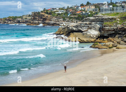 Einsame männliche Fischer Fischen mit Angelrute vom Sandstrand Bronte Beach in Sydney NSW Australien. Stockfoto