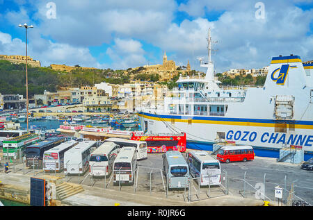 GHAJNSIELEM, MALTA - 15. JUNI 2018: Zahlreiche touristische Busse sind am Fährhafen der Insel Gozo, die große Ro-Ro-Fähre und Lourdes Kapelle geparkten Stockfoto