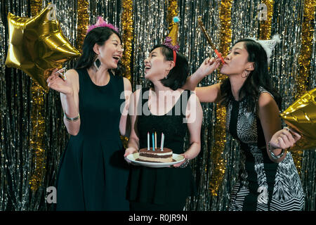 Gerne Freunde feiern Geburtstag mit Kuchen im Night Club. Junge Damen tragen Hüte Spaß mit Gebläse und glod Star ballons. Schöne cheerfu Stockfoto