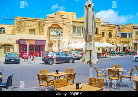 XAGHRA, MALTA - 15. Juni 2018: Die Tabellen der Outdoor Cafe in zentraler Platz mit Blick auf die alten Gebäude mit Geschäften und Restaurants, am 15. Juni in Xa Stockfoto