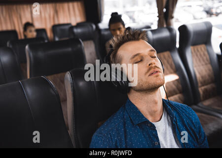 Erwachsenen Mann in Kopfhörer Musik hören und schlafen während der Fahrt im Bus Stockfoto