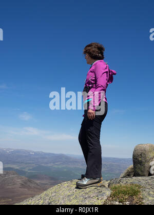 Eine reife Lady mit Blick auf die schottische Landschaft von einem Aussichtspunkt hoch auf den Hügeln bei einer Wanderung Stockfoto