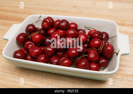 Nahaufnahme von Haufen von reifen Kirschen mit Stängeln und Blättern. Große Sammlung von frischen roten Kirschen. Reife Kirschen Hintergrund. Stockfoto