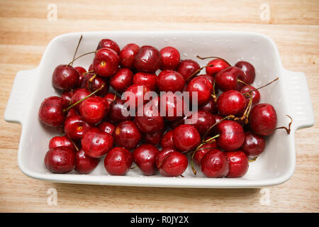 Nahaufnahme von Haufen von reifen Kirschen mit Stängeln und Blättern. Große Sammlung von frischen roten Kirschen. Reife Kirschen Hintergrund. Stockfoto