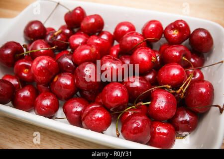Nahaufnahme von Haufen von reifen Kirschen mit Stängeln und Blättern. Große Sammlung von frischen roten Kirschen. Reife Kirschen Hintergrund. Stockfoto