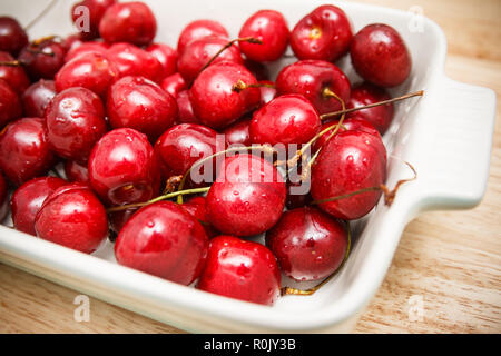 Nahaufnahme von Haufen von reifen Kirschen mit Stängeln und Blättern. Große Sammlung von frischen roten Kirschen. Reife Kirschen Hintergrund. Stockfoto