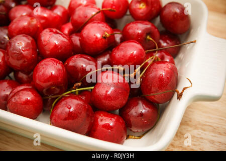 Nahaufnahme von Haufen von reifen Kirschen mit Stängeln und Blättern. Große Sammlung von frischen roten Kirschen. Reife Kirschen Hintergrund. Stockfoto