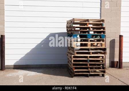 Holz Versand Paletten gestapelt gegen Gebäude Garagentor Stockfoto