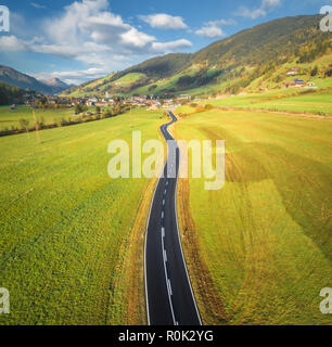Luftaufnahme von der Straße im Tal in den Dolomiten, Italien. Blick von oben auf die perfekte Asphalt Fahrbahn, Wiesen mit grünem Gras, Dorf im Herbst. Hohe Stockfoto