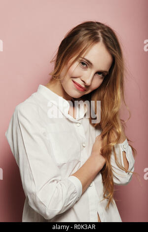 Portrait von ziemlich kaukasische Frau mit langem Haar, ein weißes Hemd auf rosa Hintergrund Stockfoto