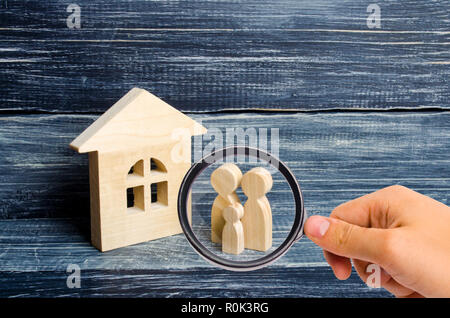 Lupe betrachtet die Familie steht in der Nähe des Hauses. Hölzerne Figuren von Personen stehen in der Nähe ein Holzhaus. Das Konzept von ein paar in Stockfoto