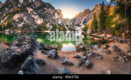 Steine an der Küste von Pragser See bei Sonnenaufgang im Herbst in den Dolomiten, Italien. Landschaft mit Bergen, Wasser mit Reflexion, Bäume im Herbst. Reisen in Stockfoto