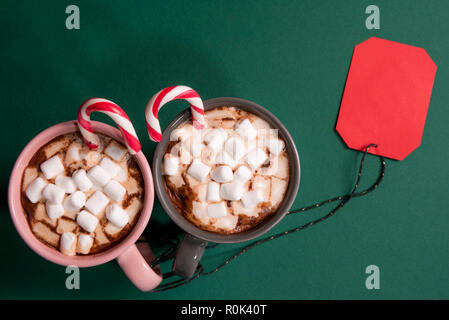 Rotes Papier tag mit einem grünen Zeichenkette von zwei Schalen mit heißer Schokolade und mini Marshmallows und zuckerstangen gebunden, am grünen Tisch Stockfoto
