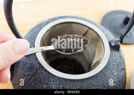 Close-up Esslöffel gourmet Lose schwarzer Tee und Gusseisen Teekanne. Schöne Textur. Stockfoto