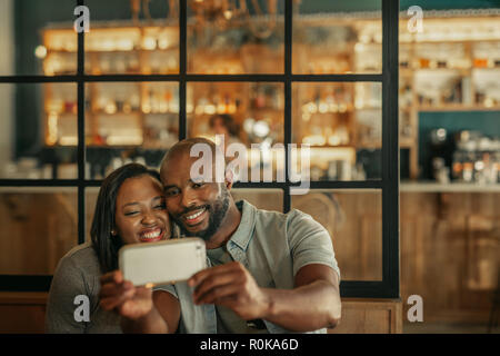Lächelnden jungen afrikanischen Paar ein selfie zusammen während der Sitzung eine Tabelle in eine trendige Bar Stockfoto