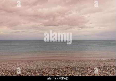 Dämmerung am Meer mit einem Kieselstrand und dramatische Wolken. Stockfoto