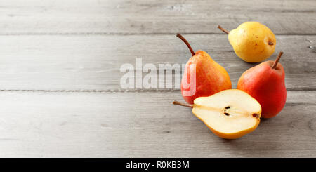 Ganze drei reife rote und gelbe Birnen und einem Schnitt in der Hälfte auf grau Holz Bretter. Banner Größe mit Platz für Text auf der linken Seite. Stockfoto