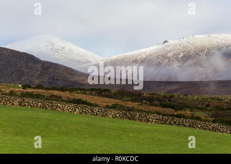 Slieve Donard und Chimney Rock Berg im hellen Schnee in der Ferne über grünes Feld und Trockenmauer gesehen. Mourne Mountains, N. Irland. Stockfoto