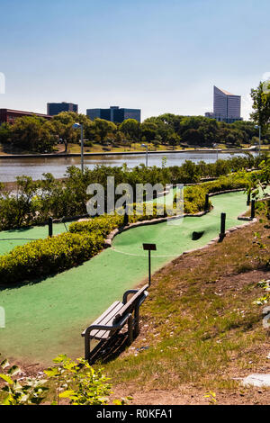 Eine minigolf Kurs neben den Arkansas River mit Stadt Gebäude im Hintergrund läuft. River Walk am gegenüberliegenden Ufer. Wichita, Kansas, USA. Stockfoto