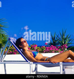 Junge Frau mit blauen Bikini Sonnenbaden auf Sonnenliegen am Pool, Guadeloupe, Französisch Westindien, Stockfoto