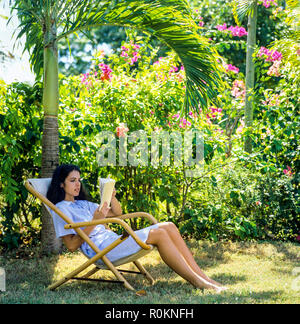 Junge Frau im Liegestuhl sitzen und ein Buch lesen, einen tropischen Garten, Guadeloupe, Französisch Westindien, Stockfoto