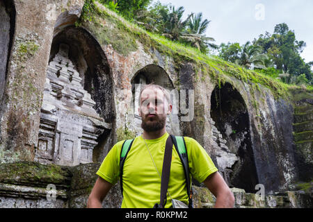 Von hinten ein Mann stand allein vor der alten Heiligen Königsgräber Gunung Kawi. Der Mensch ist die traditionelle Sarong und weiß Top gekleidet. Niemand herum. Stockfoto