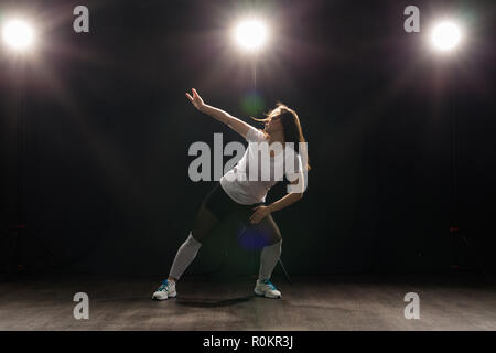 Dance, Hip Hop, Jazz Funk und Personen Konzept - flexible junge Frau tanzen in der Dunkelheit unter dem Licht Stockfoto