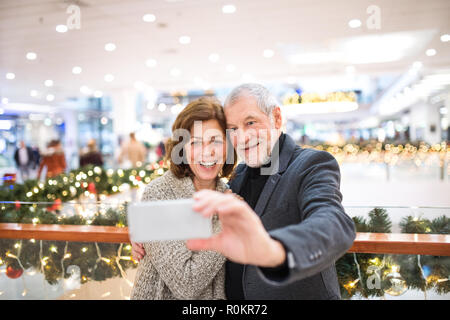 Senior Paar mit Smartphone unter selfie im Einkaufszentrum zur Weihnachtszeit. Stockfoto