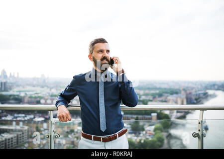 Ein Porträt der Geschäftsmann mit Smartphone stehend gegen London Panorama. Stockfoto