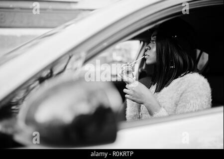 Afrikanische amerikanische Frau im lila Kleid und der Kappe an gelben Auto gestellt und zieht ihre Lippen. Stockfoto